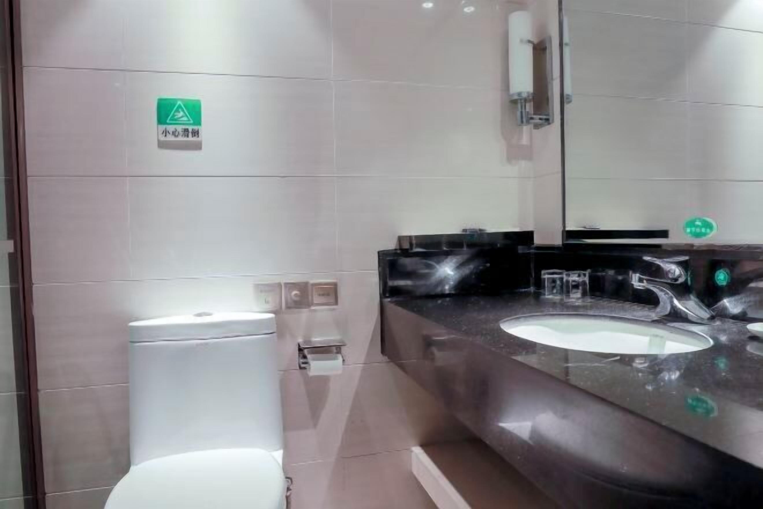 Ein modernes Badezimmer mit Toilette, Waschbecken und Spiegel. An der Wand befindet sich ein grünes Schild und ein Handtrockner.
