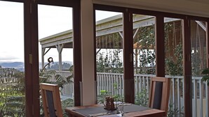 A wooden deck with a table and chairs, overlooking a garden and mountains. - Atea Lodge (Coromandel)