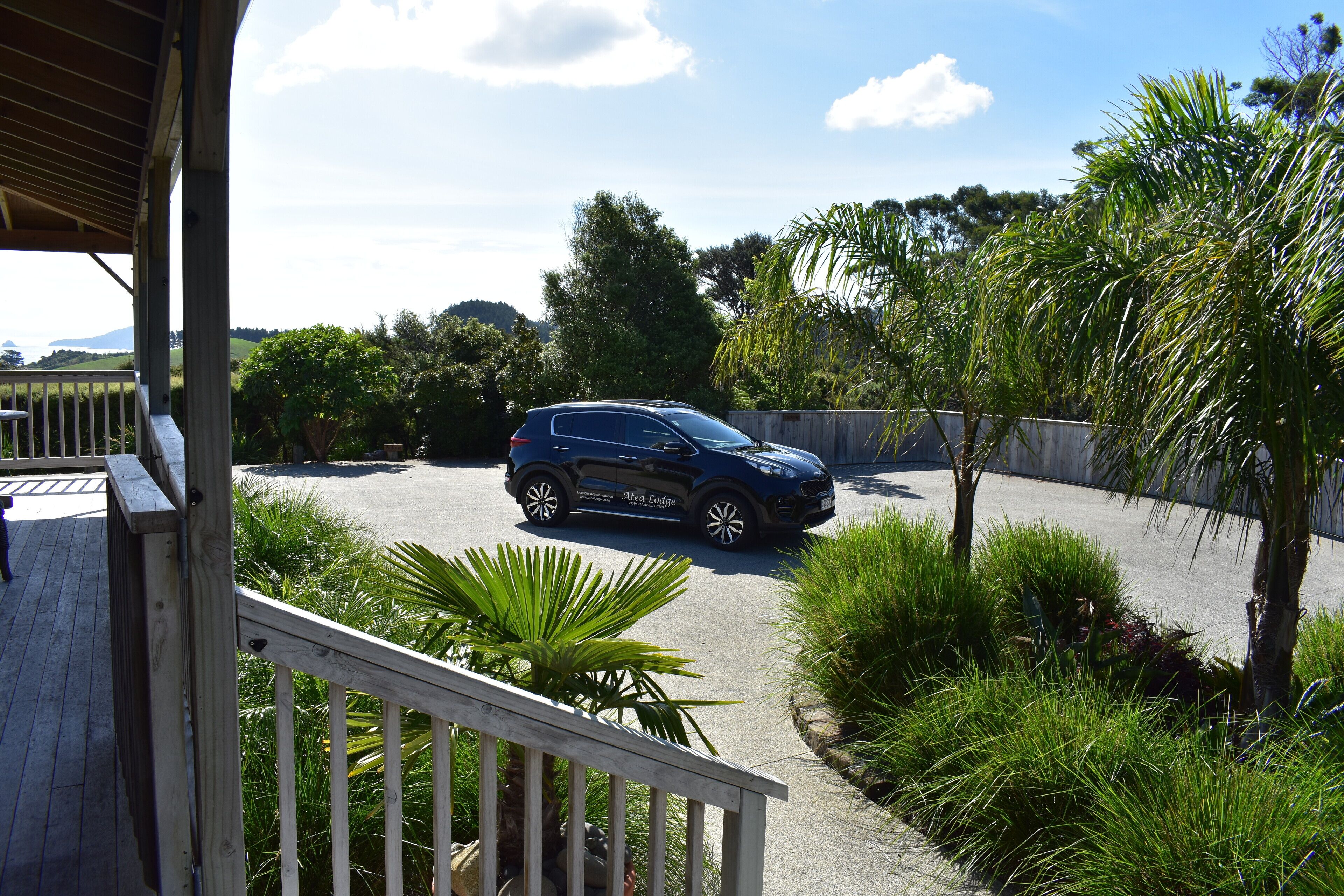 A blue SUV parked on a driveway with a wooden deck and lush greenery in the background.