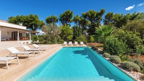 A swimming pool with lounge chairs, surrounded by trees and a building with a covered patio. - Villa Chiara by Perle di Puglia (Ruffano)