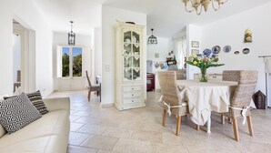 A spacious living area with a white sofa, a dining table with wicker chairs, a cabinet, and a chandelier. - Villa Chiara by Perle di Puglia (Ruffano)