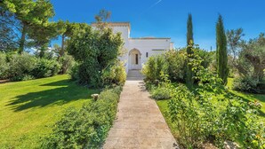 A pathway leading to a white building with a central archway, surrounded by lush greenery and tall trees. - Villa Chiara by Perle di Puglia (Ruffano)