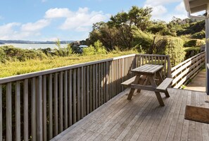 A wooden deck with a picnic table and a view of a body of water and hills. - Russell Top 10 Holiday Villas (Russell)