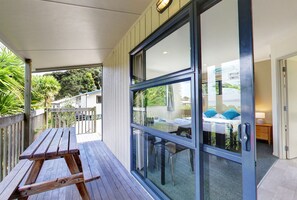 A wooden deck with a table and chairs, a glass door leading to a room with a bed and a nightstand, and a view of the outdoors. - Russell Top 10 Holiday Villas (Russell)