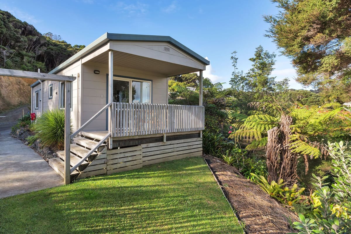 A single-story house with a covered porch, a small front yard, and a hillside backdrop.