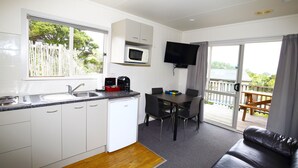 A compact kitchen with a microwave, sink, and a dining area with a table and chairs. - Russell Top 10 Holiday Villas (Russell)