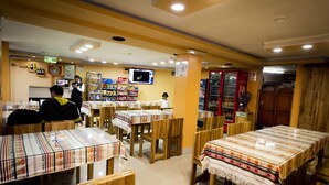 A restaurant with wooden tables and chairs, a TV screen, and shelves with bottles and snacks.