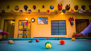 A pool table with balls in play, surrounded by various masks on the wall.