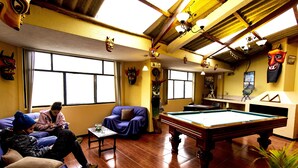 A room with a pool table, sofas, and a ceiling with wooden beams.