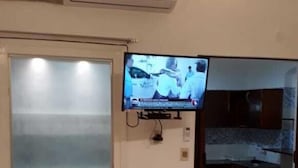 Een woonkamer met een flatscreen televisie aan de muur, een schuifdeur met glas en een betegelde vloer.