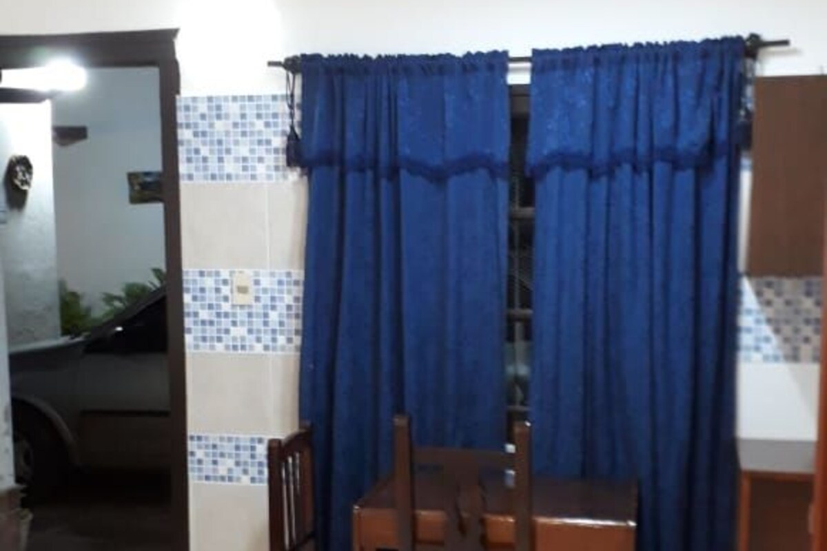 Een gezellig eetgedeelte met een tafel, stoelen, blauwe gordijnen en een betegelde spatwand.