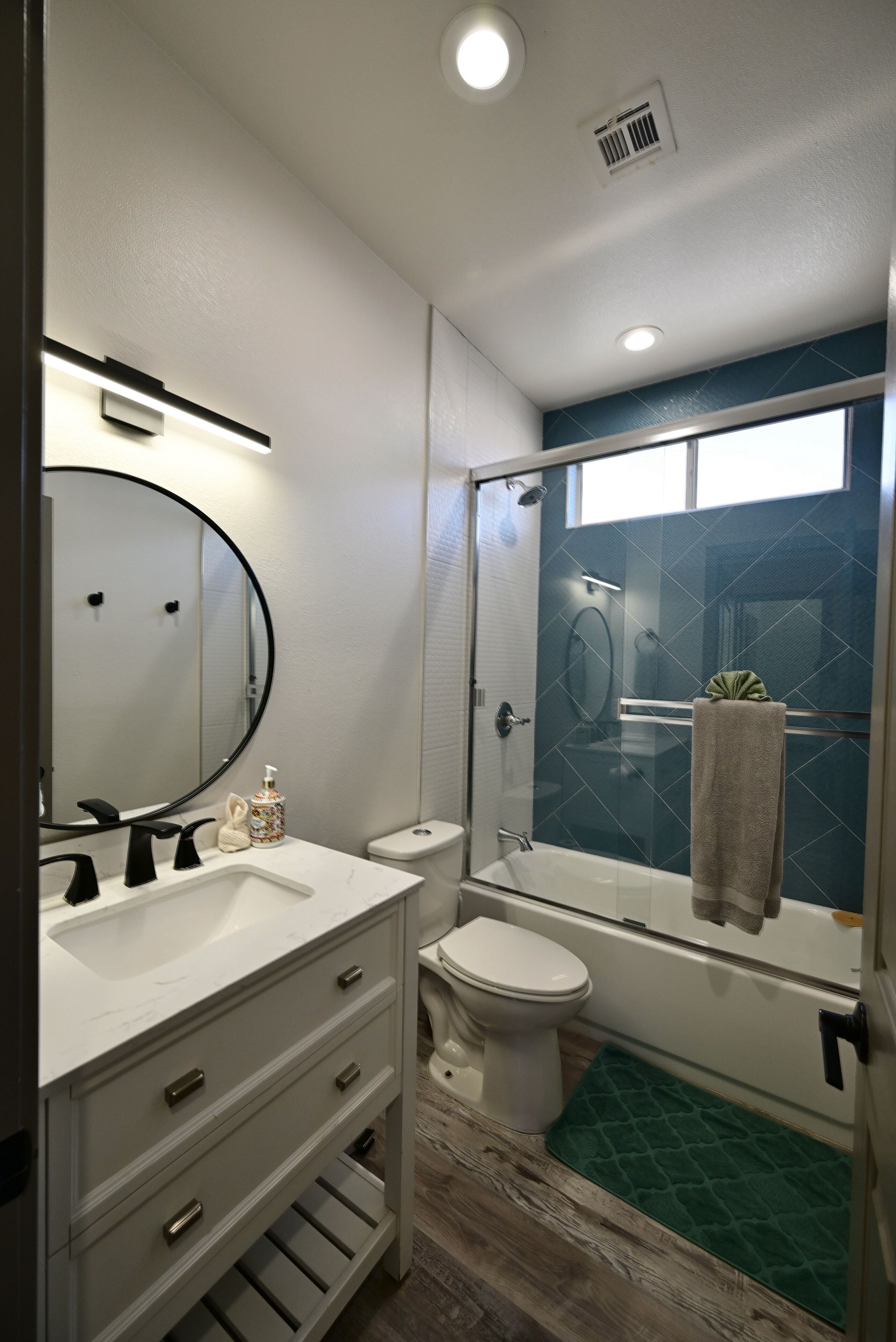 A modern bathroom with a white vanity, a round mirror, a toilet, and a glass-enclosed shower area.
