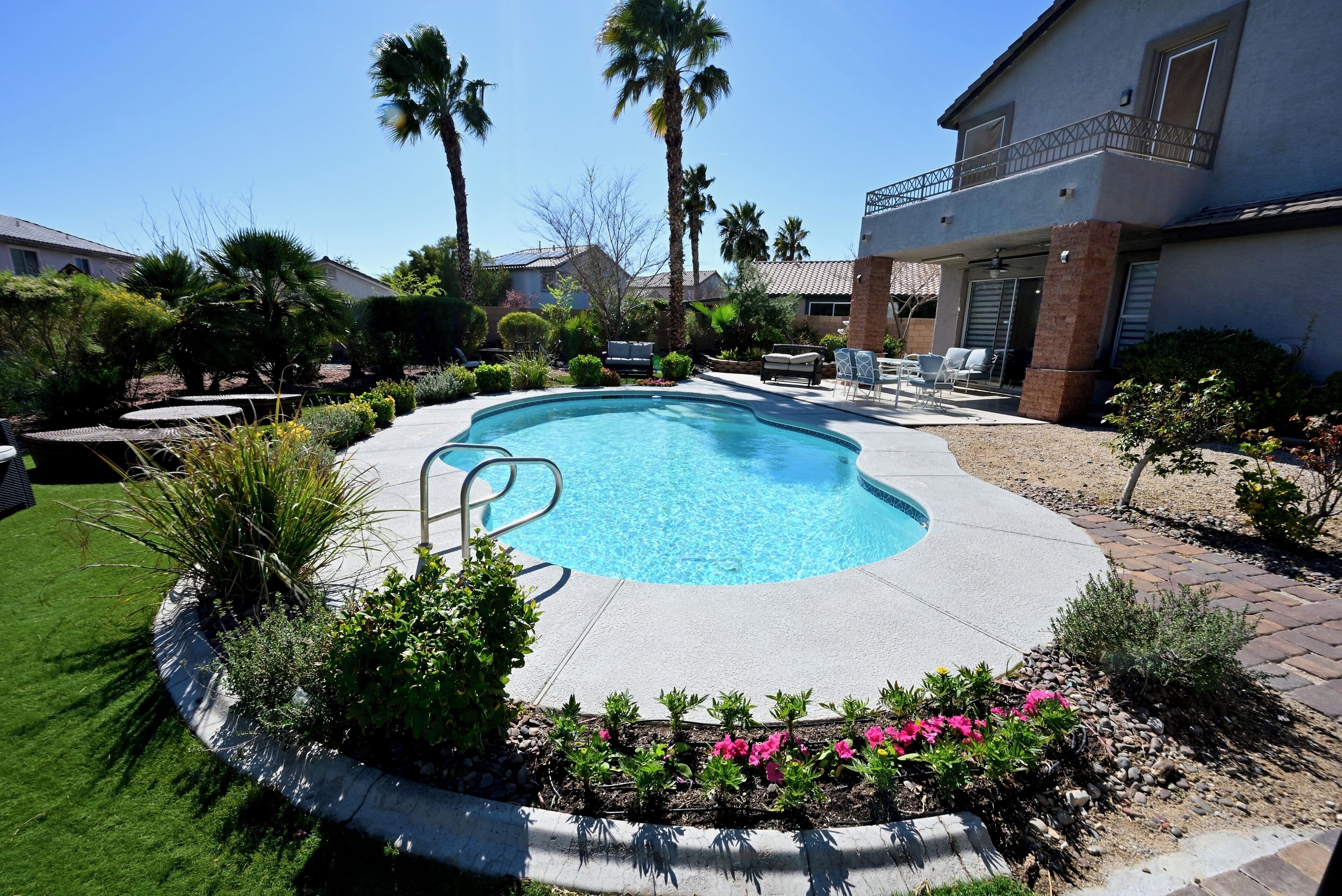 Una piscina rodeada por un jardín ajardinado con palmeras y un patio con mobiliario de exterior.