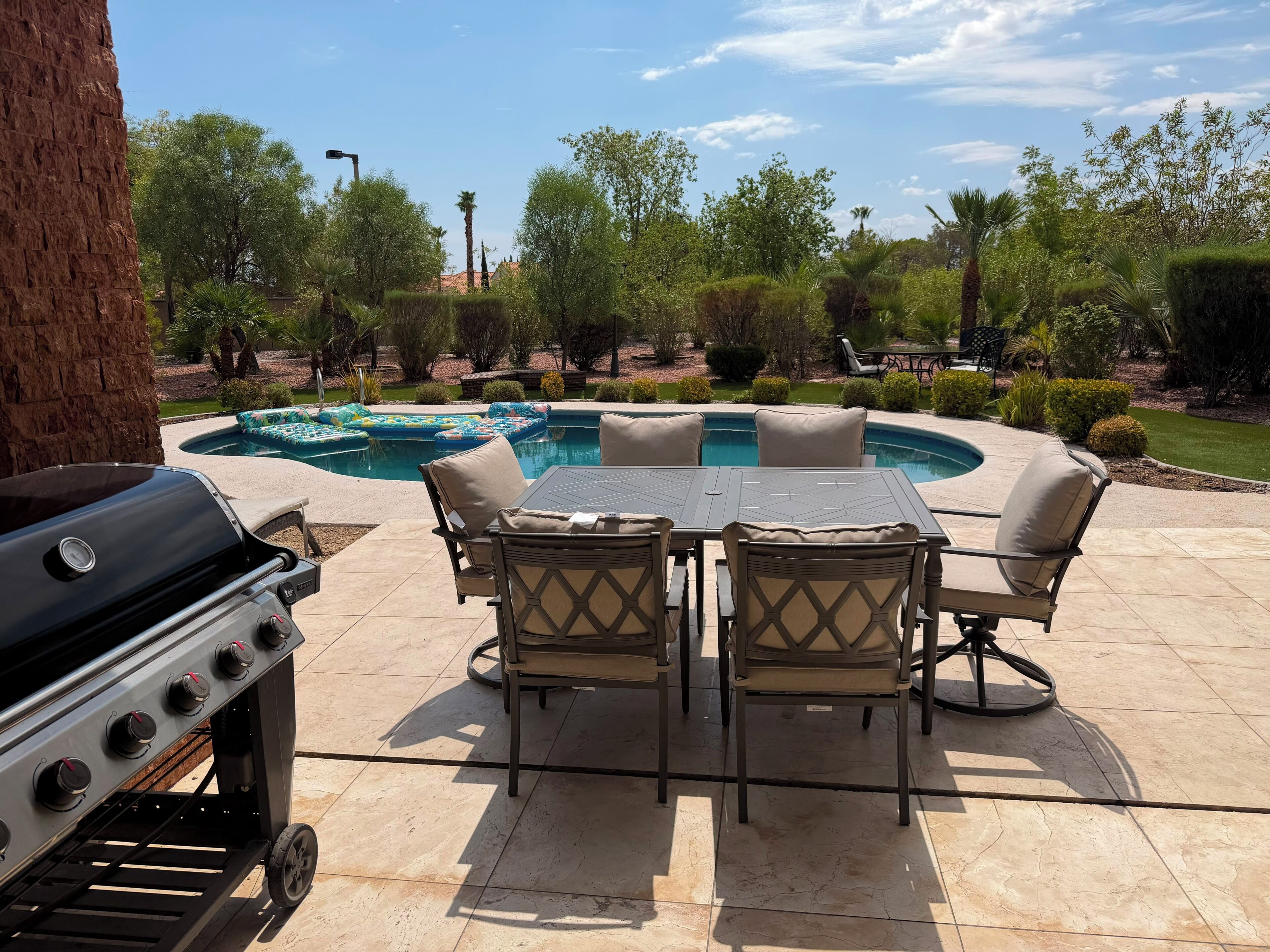 Un patio al aire libre con una parrilla, una piscina y una mesa con sillas.