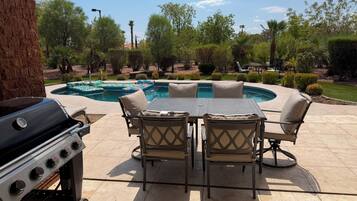 Un patio al aire libre con una parrilla, una piscina y una mesa con sillas.