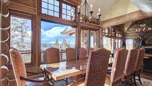 A dining area with a large wooden table and patterned chairs, large windows with a mountain view, and a chandelier. - Ten Mile Estate: Private Breckenridge Home with Hot Tub and Views (Breckenridge)