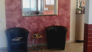A room with a pink wall, a mirror, two chairs, a small table with a vase, and a trash bin. - Haus Hamburg (Bad Fuessing)