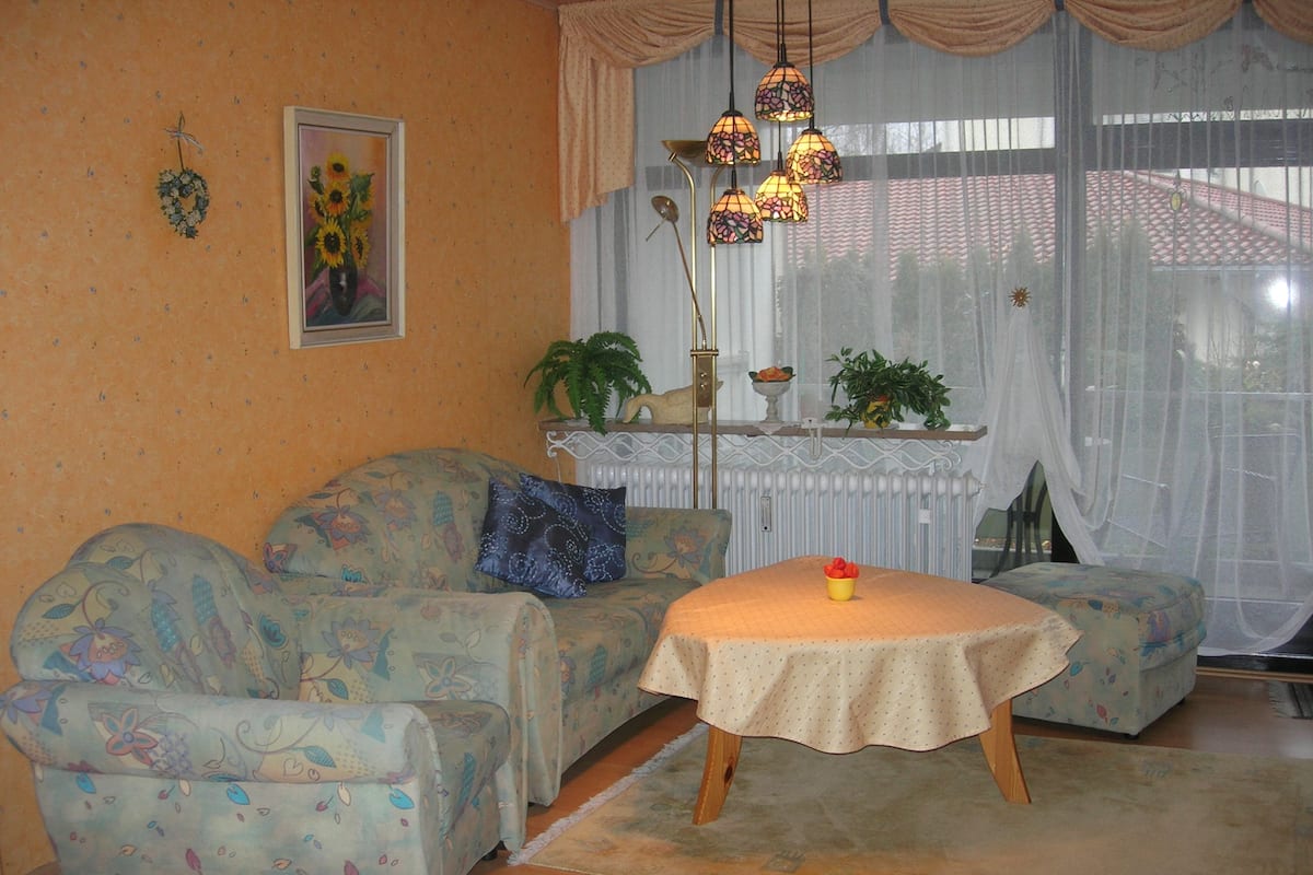 A cozy living room with patterned sofas, a small table with a bowl, and hanging lamps.