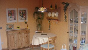 A dining area with a round table, wooden chairs, a hanging light fixture, a cabinet with glassware, and a wicker basket. - Haus Hamburg (Bad Fuessing)