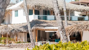 Un hotel frente a la playa con estructuras de techo de paja, mobiliario exterior y un muro de piedra.
