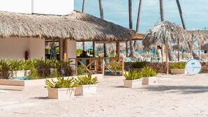 Un hotel frente a la playa con estructuras de techo de paja, palmeras y una zona de piscina.