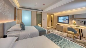 Habitación de hotel con dos camas, un escritorio, una silla, un televisor y una mesita con un jarrón.