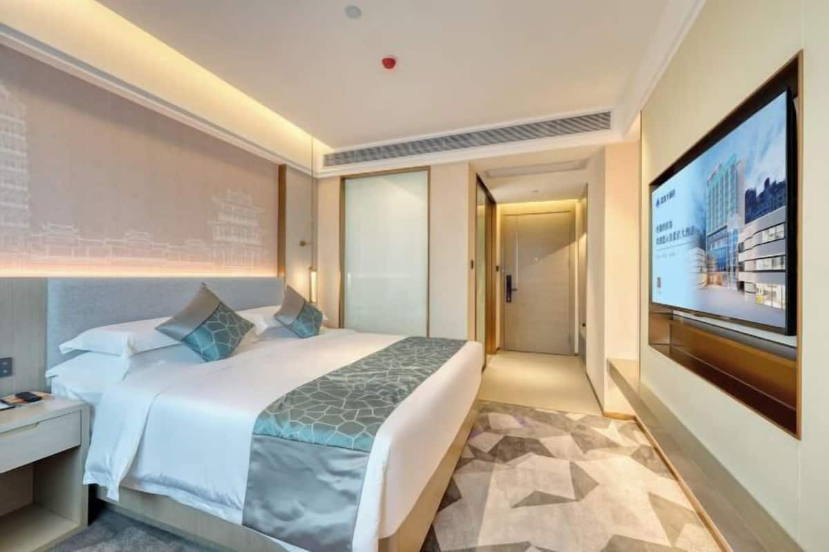 A hotel room with a bed, a nightstand, a TV, and a wall-mounted artwork.