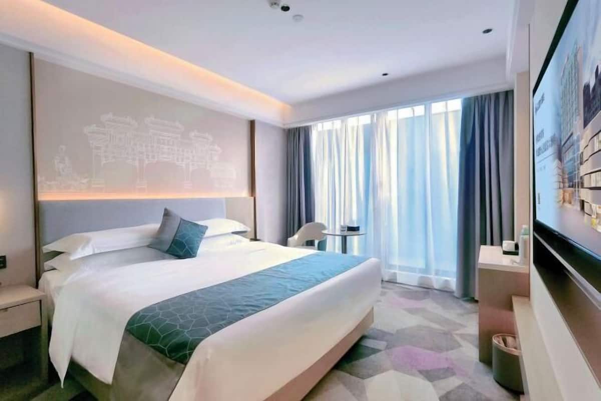 A hotel room with a large bed, a desk, a chair, a TV, and a window with curtains.