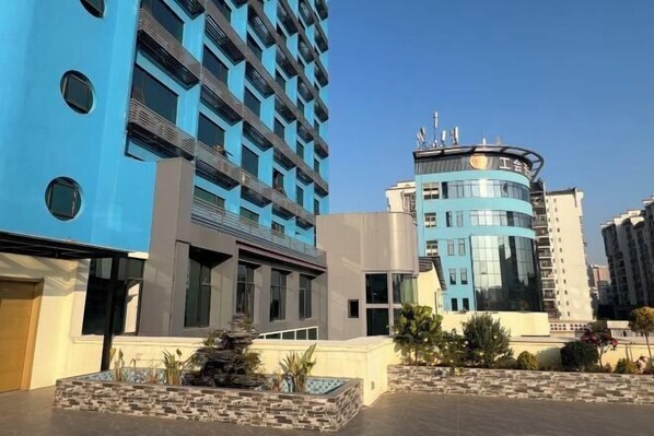 Un hotel moderno con fachada azul, una torre central circular y un patio ajardinado.