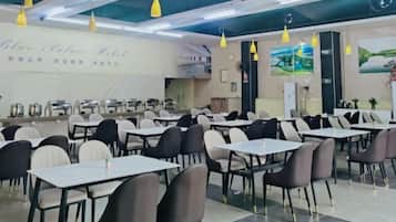 A dining area with multiple tables and chairs, a counter with food service equipment, and a wall with a landscape painting.