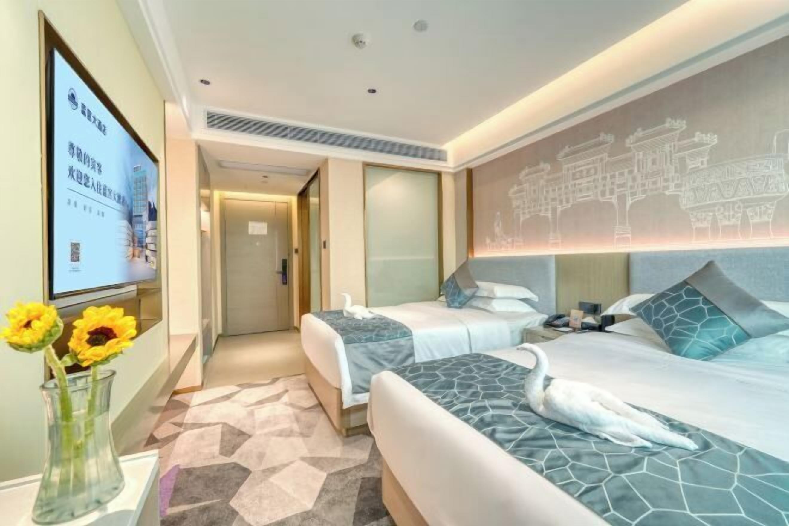 Een hotelkamer met twee bedden, een tv aan de muur, een bloemenvaas en decoratieve wand.