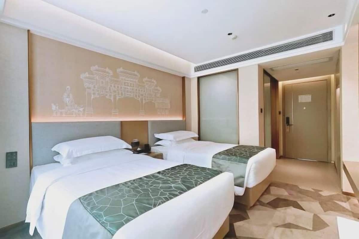 A hotel room with two beds, a wall-mounted artwork, a bedside table, and a door leading to another room.