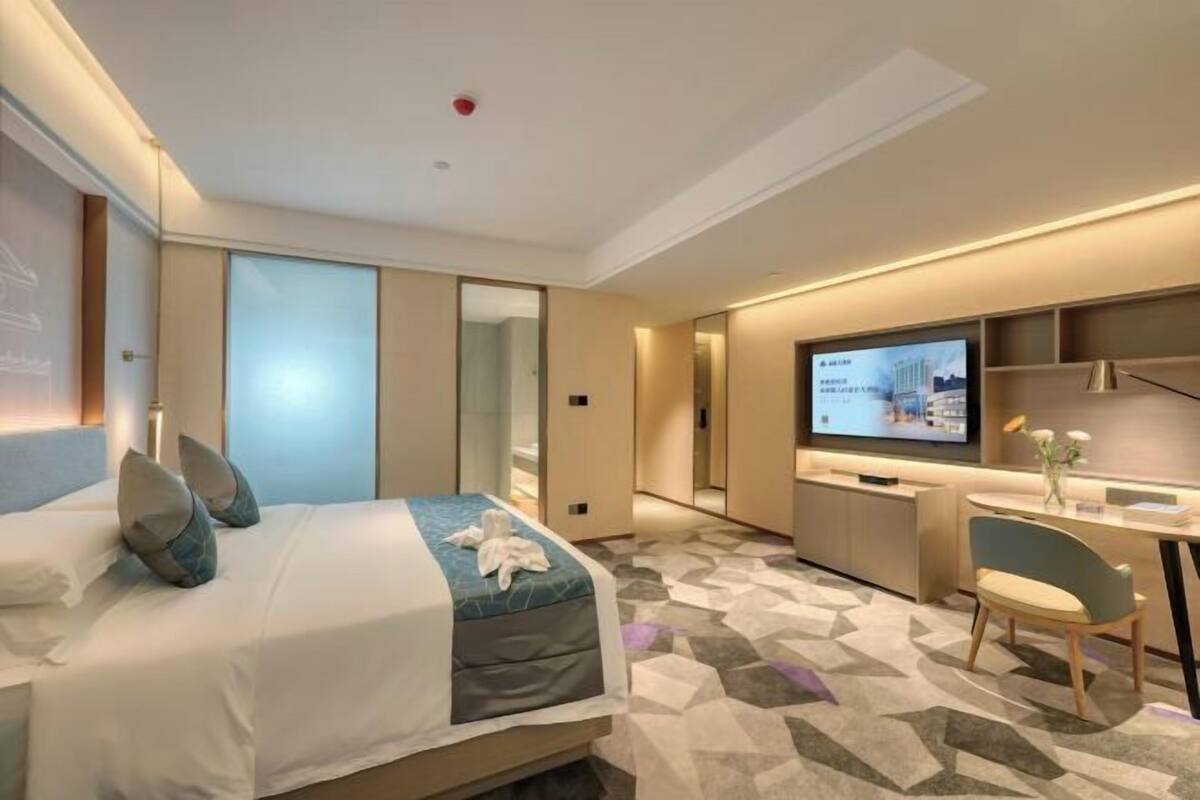 A modern hotel room with a bed, a desk, a television, and a mirror.