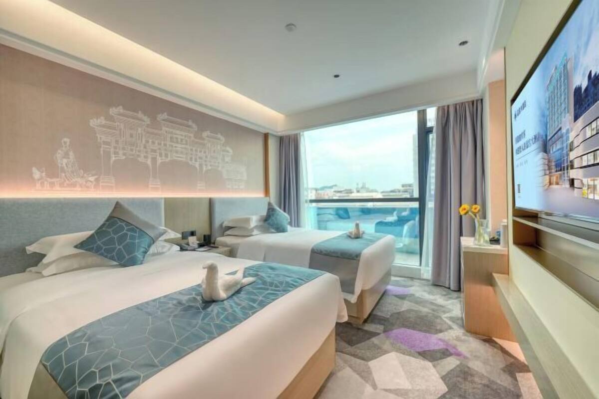 A hotel room with two beds, a large window, a view of the city, and a wall-mounted TV.