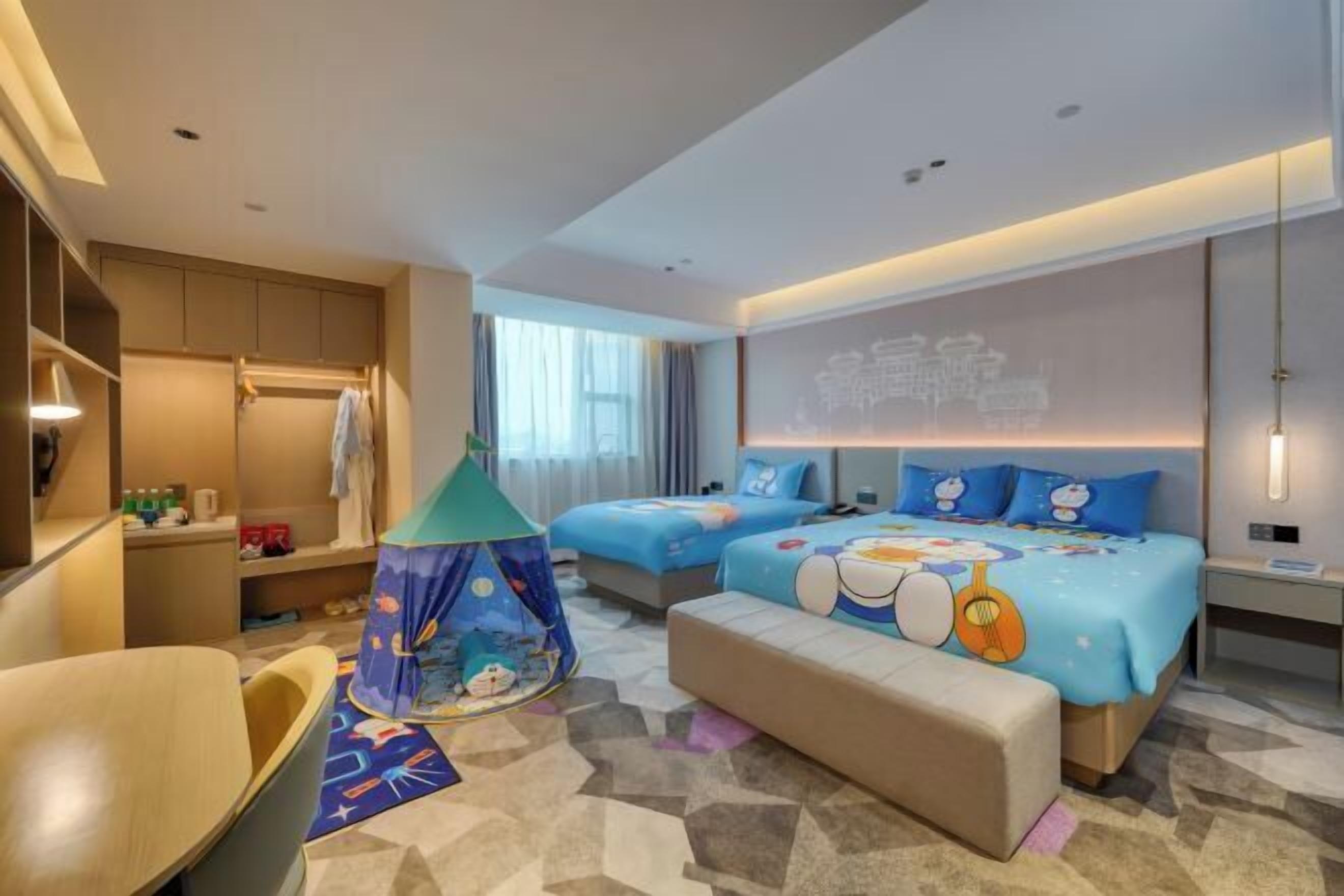 A hotel room with two beds, a play tent, a seating area, and a large window.
