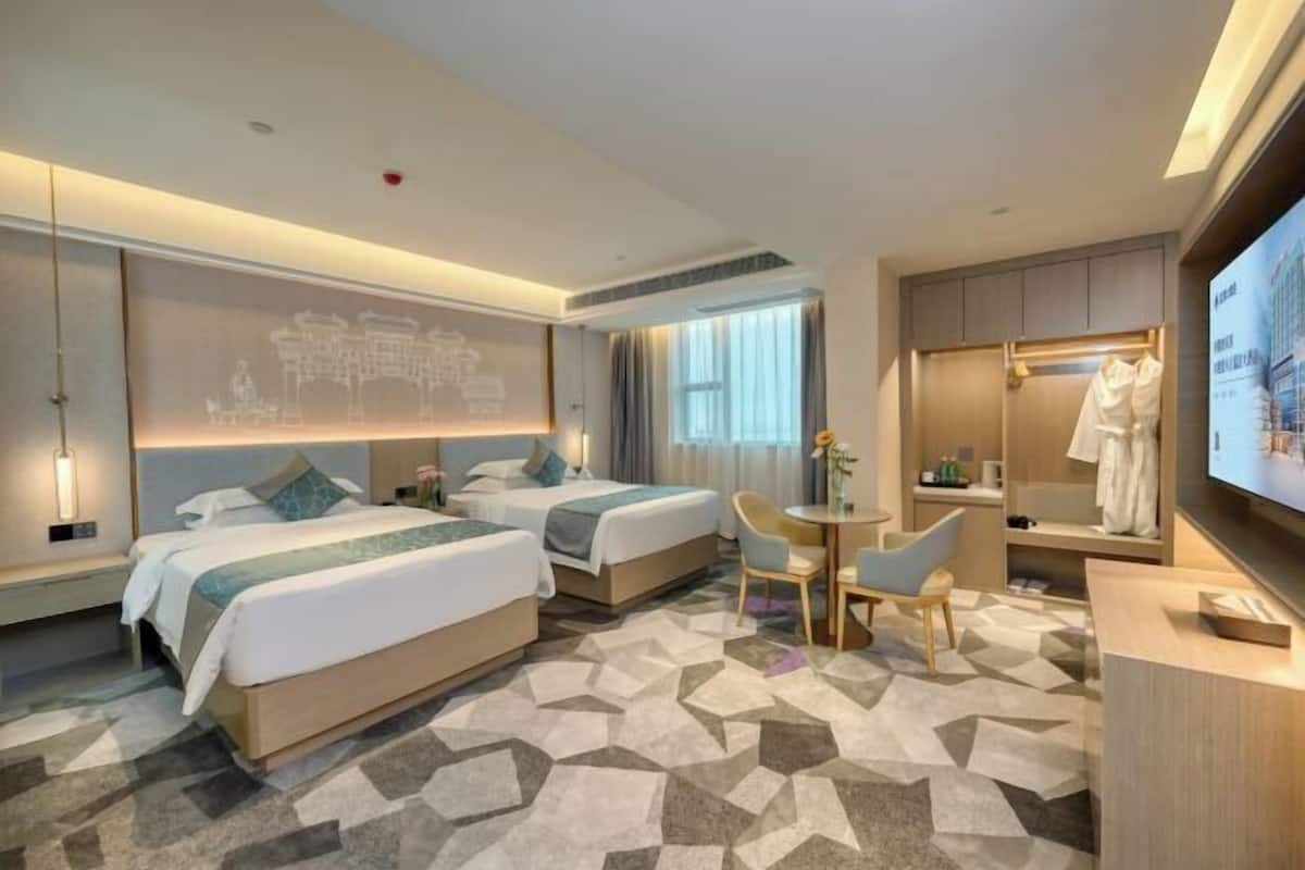A hotel room with two beds, a desk, a chair, a television, and a large mirror.