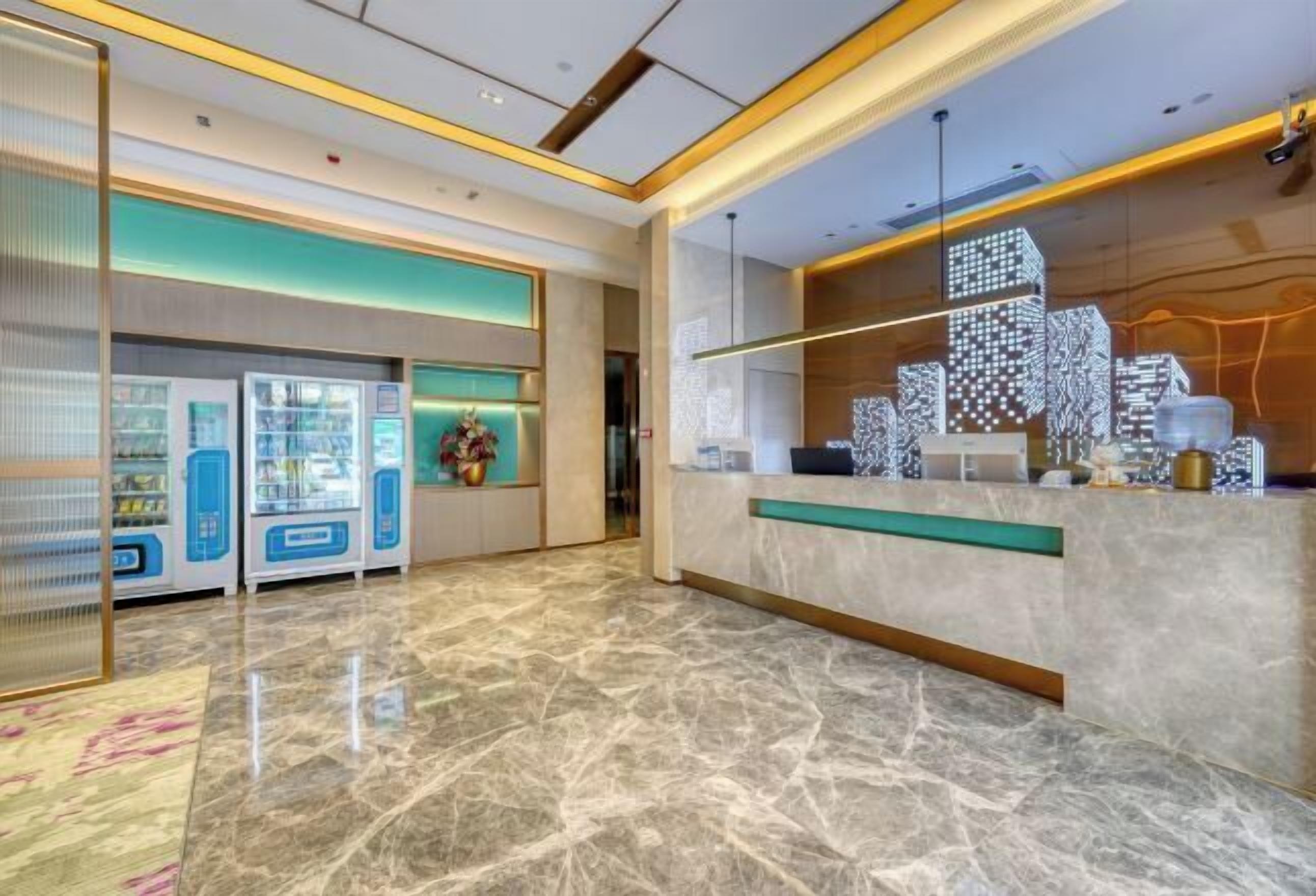 A modern hotel lobby with a marble floor, vending machines, and a reception desk with a cityscape design.