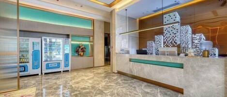 A modern hotel lobby with a marble floor, vending machines, and a reception desk with a cityscape design.