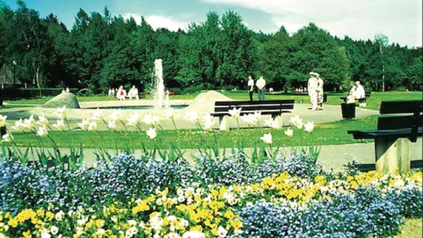 A park with a fountain, benches, and people walking. - Haus Salzburg (Bad Fuessing)