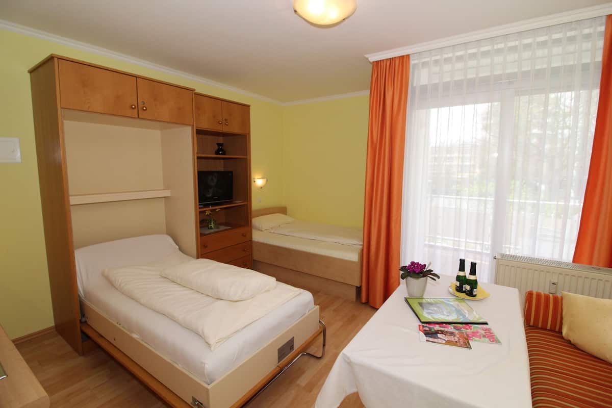 A bedroom with a bed, a desk with a chair, a wardrobe, and a window with curtains.
