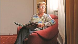 An elderly person sitting in a red armchair, reading a book. - Haus Salzburg (Bad Fuessing)