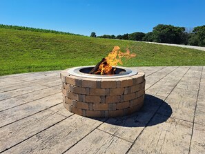 Un foyer circulaire, dont l’extérieur est en briques, entouré d’une terrasse en bois.