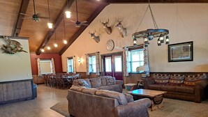 A spacious living room with a high ceiling, wooden beams, a fireplace, and a dining area with a table and chairs. - Lost Branch Lodge. Complete exterior remodel, spring 2026! (Brashear)