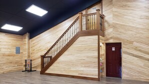 A wooden staircase with a railing, a door, and a ceiling with fluorescent lights. - Lost Branch Lodge. Complete exterior remodel, spring 2026! (Brashear)