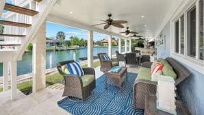 A covered outdoor seating area with wicker furniture, ceiling fans, and a view of a lake. -  Beautiful Waterfront Pool Home, Walk to Beach, Pool/PPong Tbl (Marco Island)