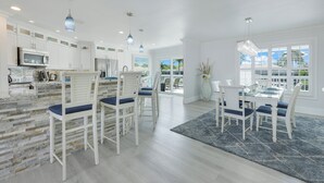 A modern kitchen with white cabinetry, a stone backsplash, and a dining area with white chairs and a blue rug. -  Beautiful Waterfront Pool Home, Walk to Beach, Pool/PPong Tbl (Marco Island)