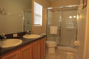 A bathroom with two sinks, a toilet, and a glass-enclosed shower. - Four Corners Area Pool Homes by ORB (Davenport)