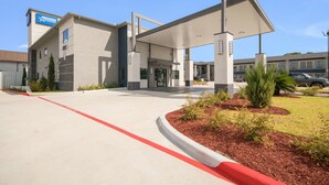 A modern building with a prominent American Express sign, a covered entrance, and a landscaped area with shrubs. - Americas Best Value Inn & Suites NE Houston Downtown I-610 (Houston)