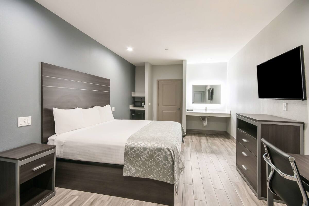 A modern hotel room with a large bed, a desk, a chair, a TV, and a wardrobe.