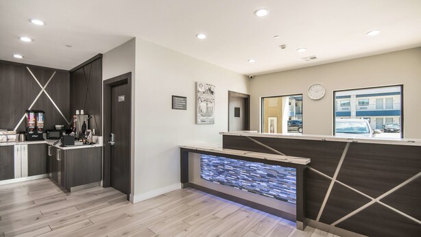 A modern hotel lobby with a reception desk, a kitchen area, and a large window with a view of the outside. - Americas Best Value Inn & Suites NE Houston Downtown I-610 (Houston)